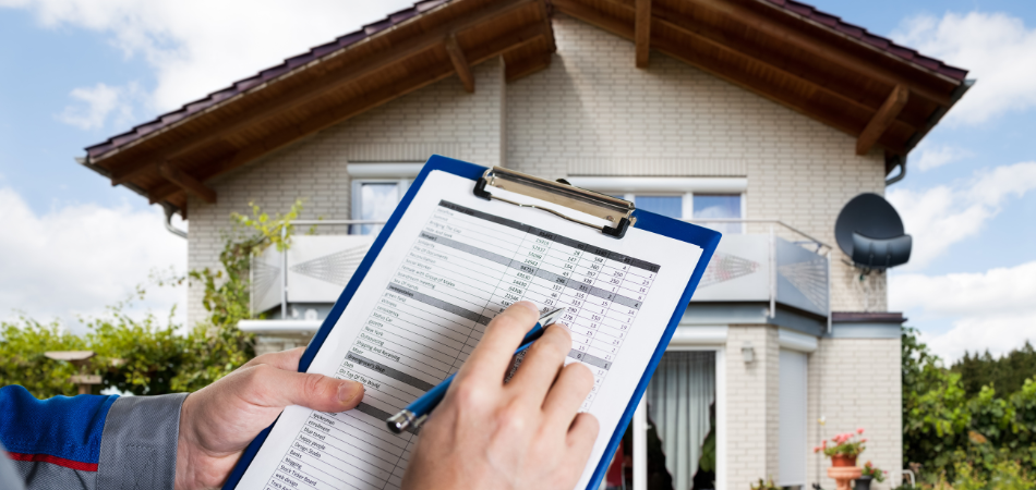 A person with a clipboard and pen in front a house, appraising it.